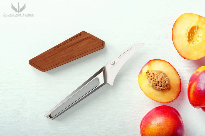 A photo of the Bird's Beak Paring Knife Peeler 3" Crusader Series NSF Certified Dalstrong beside fresh slices of peaches
