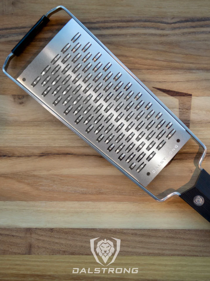 A photo of the Dalstrong Professional Ribbon Wide Cheese Grater on top of a wooden board.