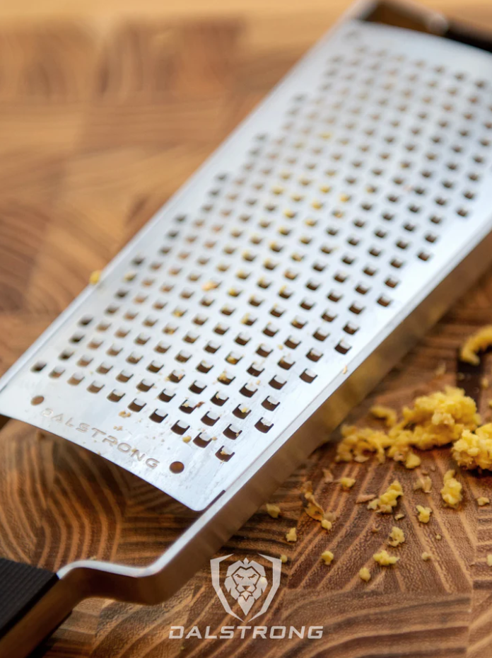 Dalstrong Professional Coarse Wide Grater on a wooden table with grated ginger on the side.