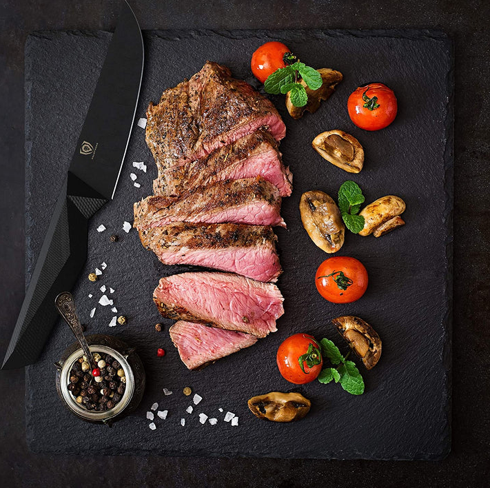 A photo of the Dalstrong Shadow Black Series Steak knife on top of a black board with a beautiful steak and vegetables beside.