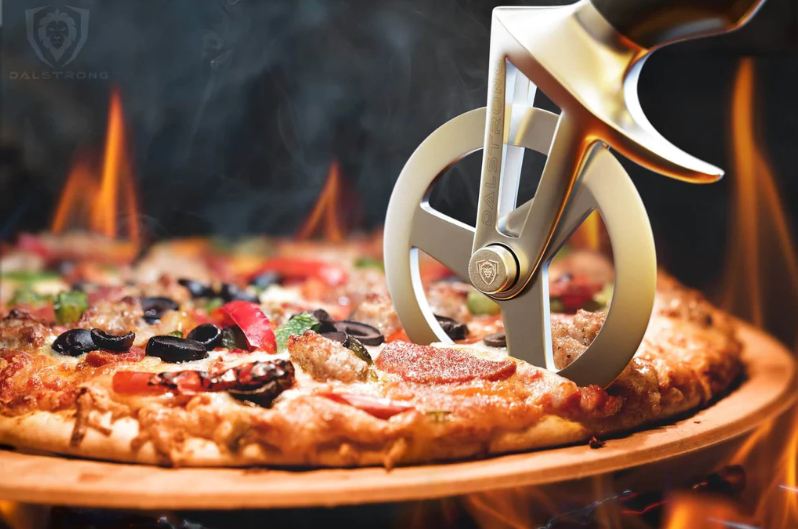 A photo of the Dalstrong Orbit Razor Pizza Wheel & Cutter slicing a pizza on a wooden board and surrounded with fire