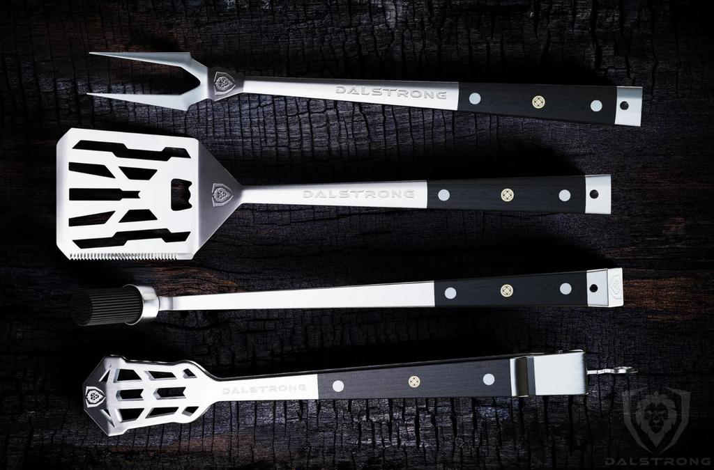 The Dalstrong Tongs, Spatula, Fork, Silicone Brush 4 Piece Premium Grill Kit on top of a burned wood