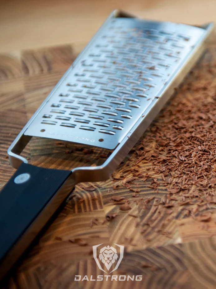 A photo of the Dalstrong Professional Ribbon Wide Cheese Grater with grated chocolate on top of the Dalstrong wooden board.