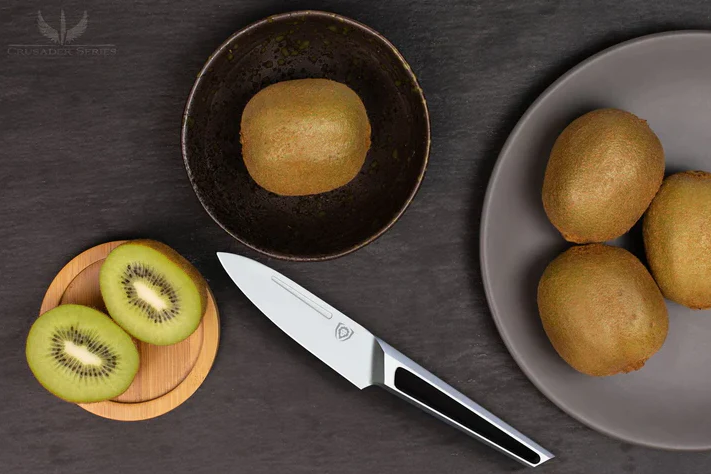 A photo of a perfectly sliced kiwi in a round wooden board with the Paring Knife 3.5" Crusader Series NSF Certified Dalstrong and four uncut kiwi beside