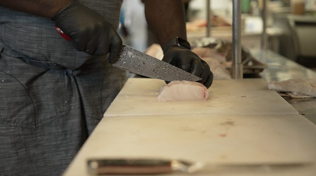 A man with gloves slicing meat using the Scorpion Series Chef's Knife 9.5"