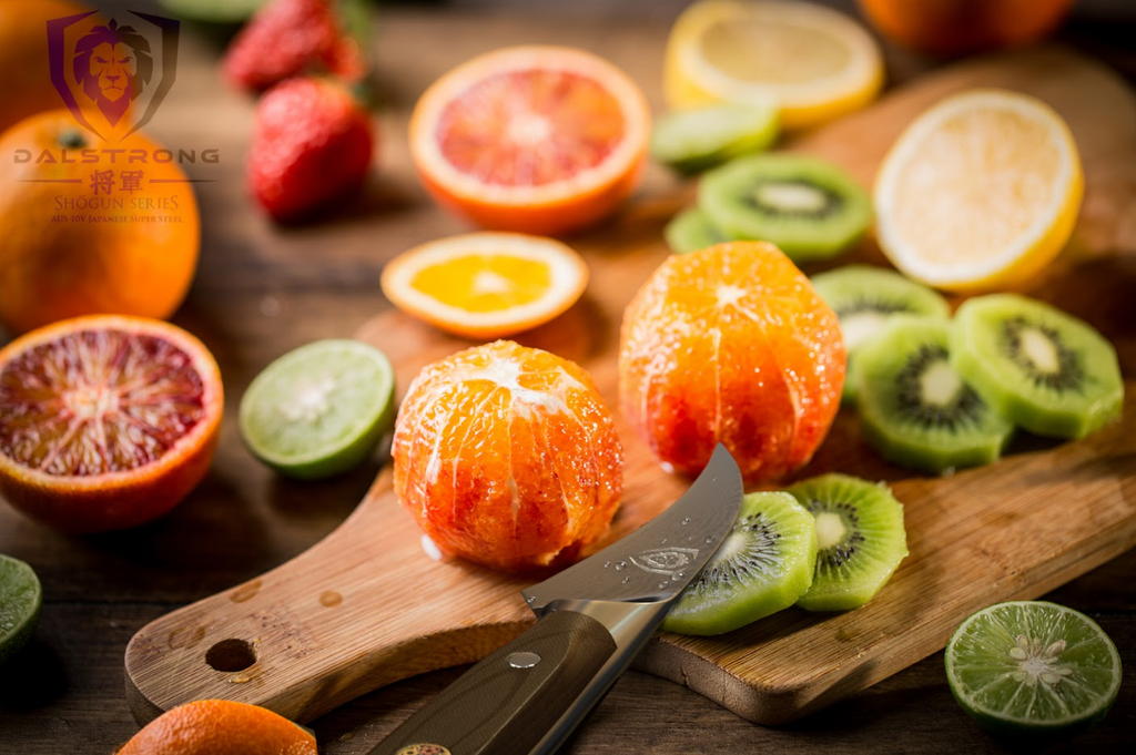 A photo of the Bird's Beak Peeling & Paring Knife 3" Shogun Series ELITE | Dalstrong with two perfectly peeled orange and slices of kiwi on top of a wooden board.