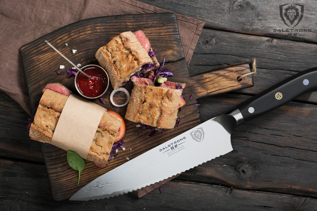 A photo of the Serrated Chef's Knife 7.5" Shogun Series ELITE | Dalstrong with a sandwich in top of a wooden board.