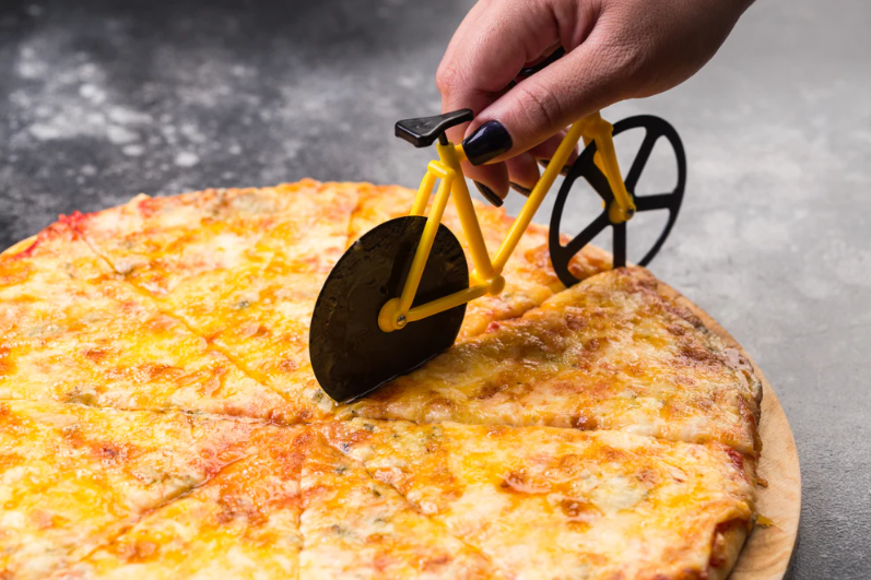 A pizza cutter in the shape of a bicycle slicing through a cheese pizza