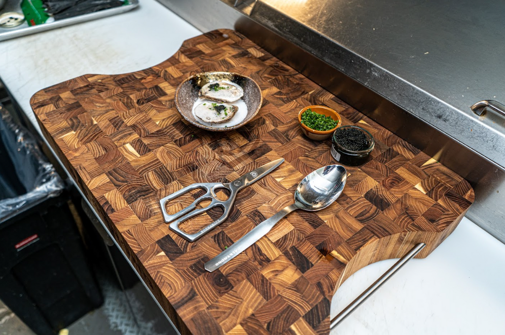 A photo of the Professional Kitchen Scissors 420J2 Japanese Stainless Steel Dalstrong beside the Professional Chef Tasting & Plating Spoon on top of a Dalstrong wooden board