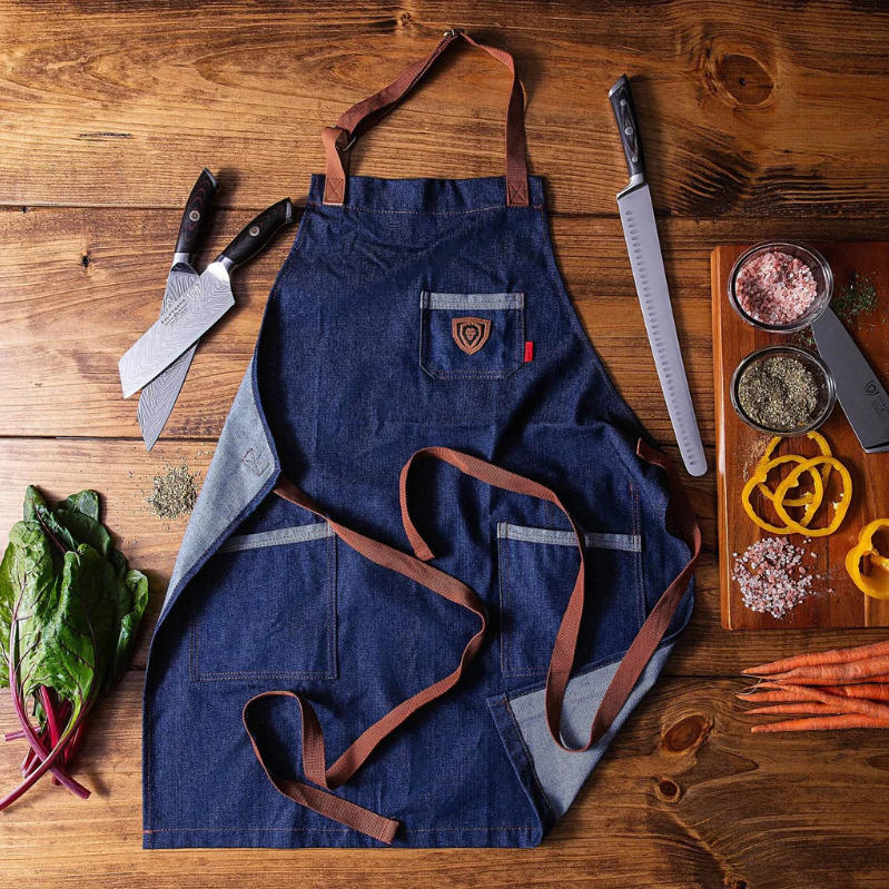 A photo of the American Legend Blue Denim Professional Chef's Kitchen Apron Dalstrong with three Dalstrong knives in each side on top of a wooden table