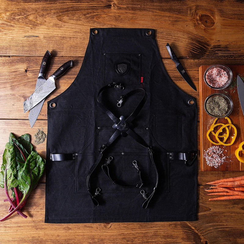 Black kitchen apron on a wooden floor next to chopped food and a kitchen knife