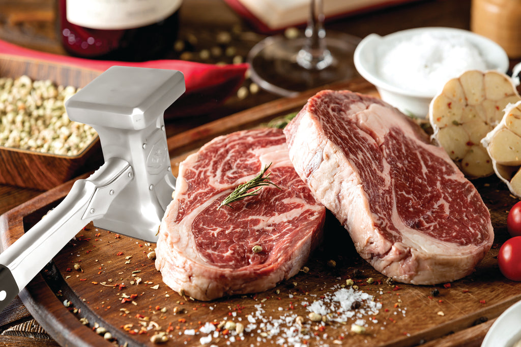 Two thick pieces of uncooked steak on a cutting board next to a meat tenderizer