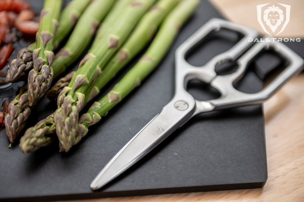 Dalstrong Kitchen Shears on a black cutting board with asparagus on the side