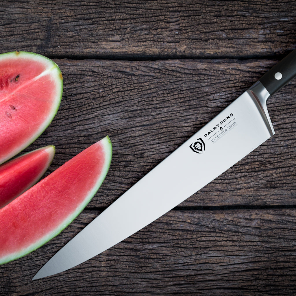 A watermelon cut in half on a wooden surface next to a sharp kitchen knife