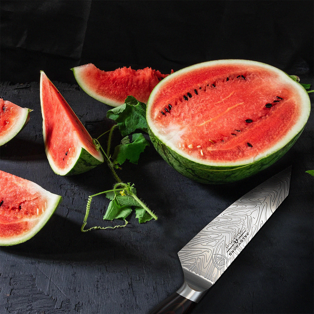 Several pieces of watermelon against a dark surface next to a chef's knife