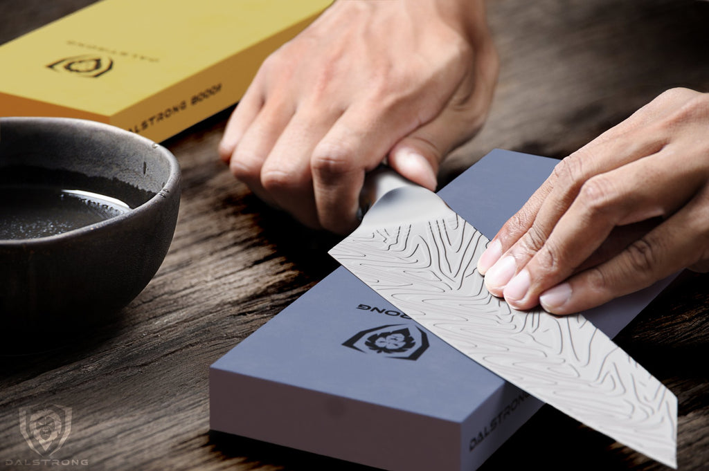 Close up of hands sharpening a kitchen knife against a blue whetstone