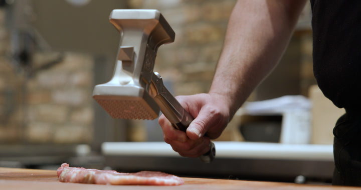 A man tenderizing a meat using the Dalstrong Dual Sided, Heavy Duty & Extra-Large Hammer Meat Tenderizer 15"