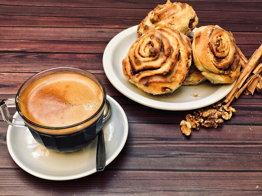 Cinnamon buns on a white plate with a cup of coffee on the side served on a dark wooden table.