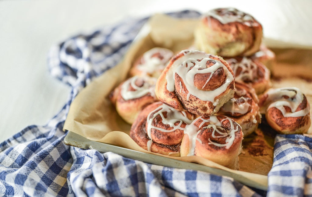 Freshly baked cinnamon rolls on a baking tray with blue checkered fabric underneath.