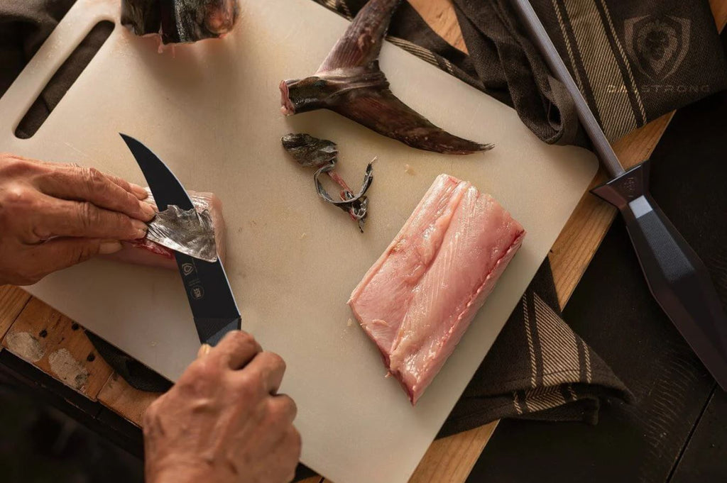 Slices of fish being filleted using Dalstrong Shadow Black Series Fillet Knife on a white cutting board with a honing rod on the side.