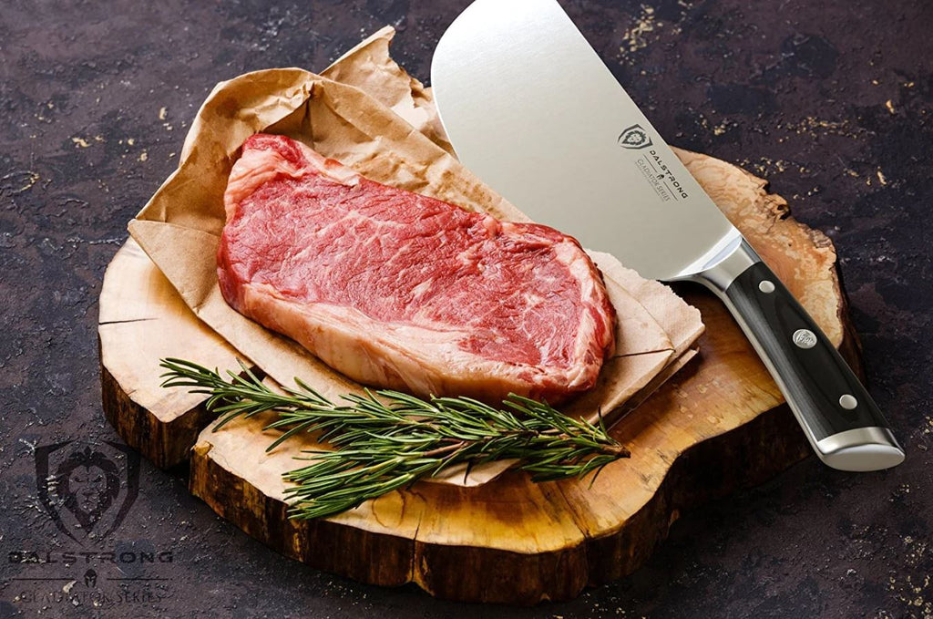 Dalstrong meat cleaver beside a slice of meat and rosemary placed on top of a wooden cutting board