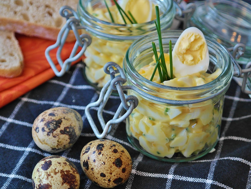 Two glass containers of creamy egg salad ready to be served with eggs on the side.