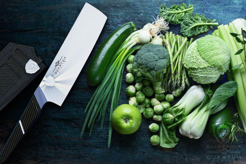 Different raw and fresh vegetables on a blue wooden table with a Dalstrong Quantum 1 Series Nakiri knife on the side.