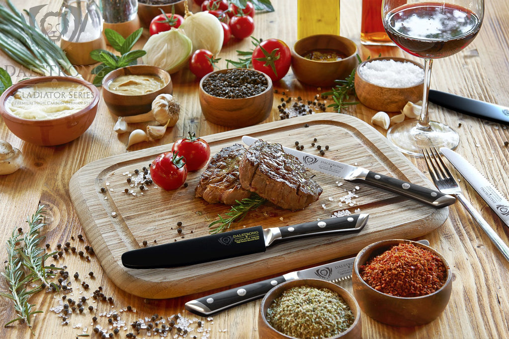 Table of food with wooden cutting board that has chopped steak and steak knives on it