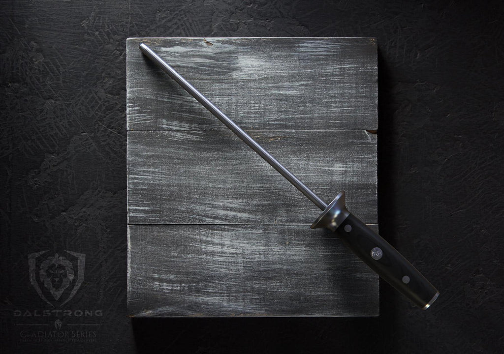 A sharpening steel with a black handle rests on a dark grey cutting board against a black background