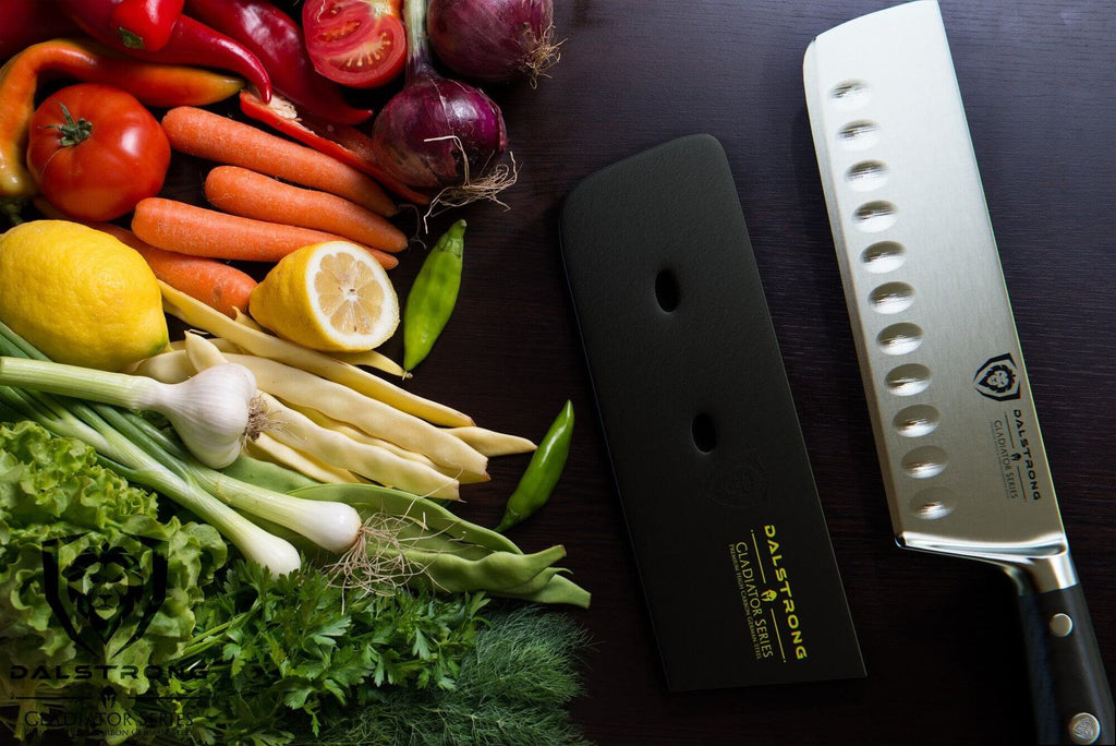 A variety of vegetables against a dark surface next to a sharp nakiri knife