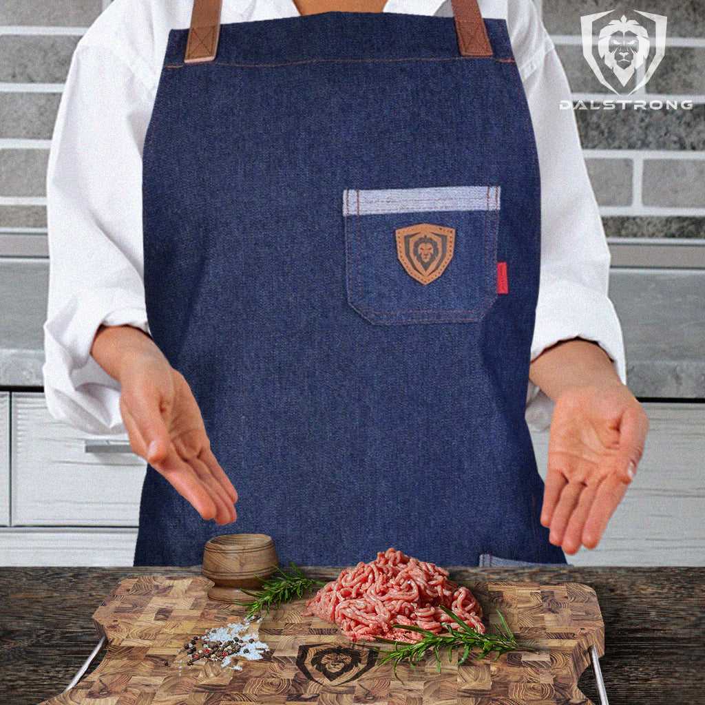 A homecook wearing a Dalstrong apron preparing raw ground beef for cooking on a Dalstrong wooden cutting board with herbs and salt.