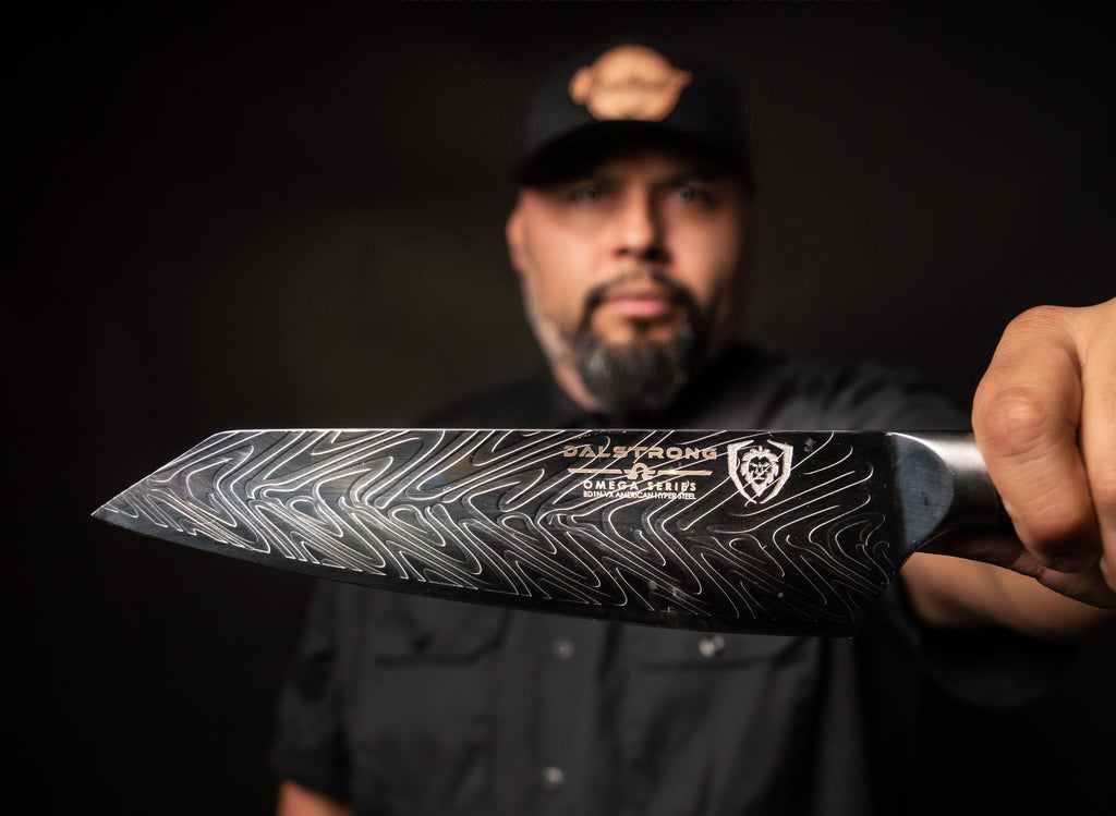Chef Steve Hernandez in black clothes and blackgrond holding a Dalstrong blade to the camera 