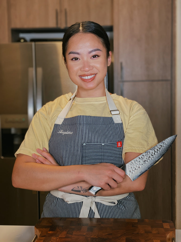 Twaedabae poses in a chef apron holding a dalstrong shogun series chef knife