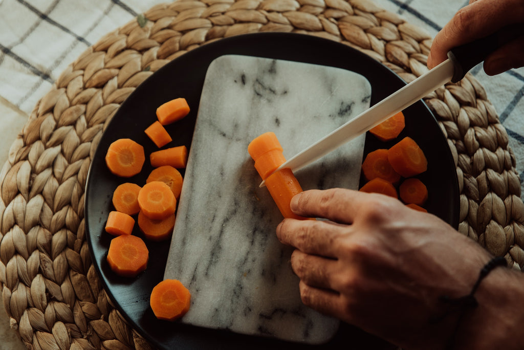 Hands of a Person Slicing Carrots on Marble Slate