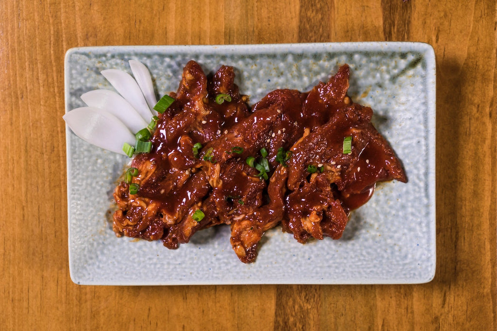 Meat covered by korean bbq sauce and green onions on top of a ceramic plate.
