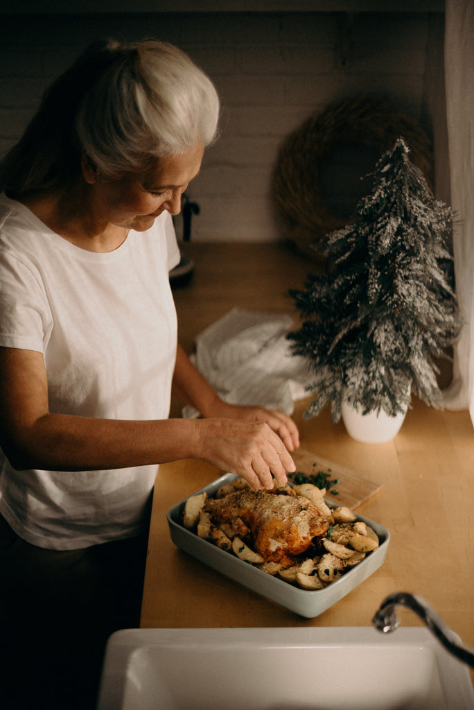 A lady garnishing a roasted chicken with with potatoes on the side on a roasting pan