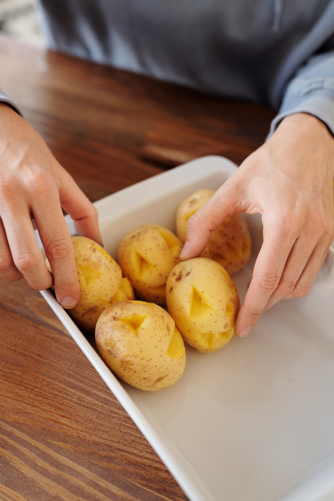 Fresh potaoes with poked holes lined up on a white baking tray