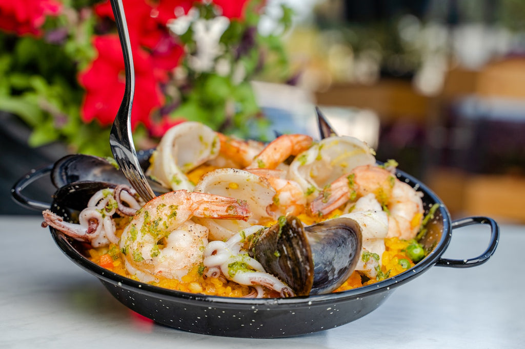 A close up shot of a black bowl full of delicious Paella garnished with different seafoods on top for a visual and appetizing look.