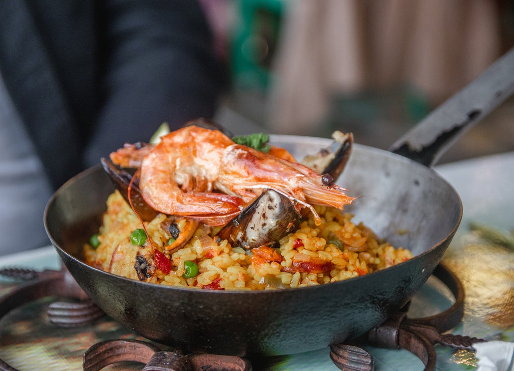 Photo of a black skillet full of visually appetizing Paella garnished with a huge shrimp on top