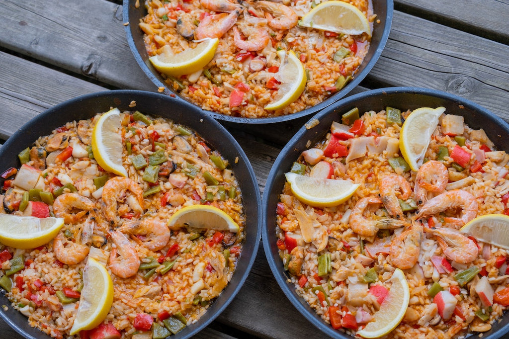 Three full plates of freshly served Paella with slices of lemon, on top of a dark wooden table