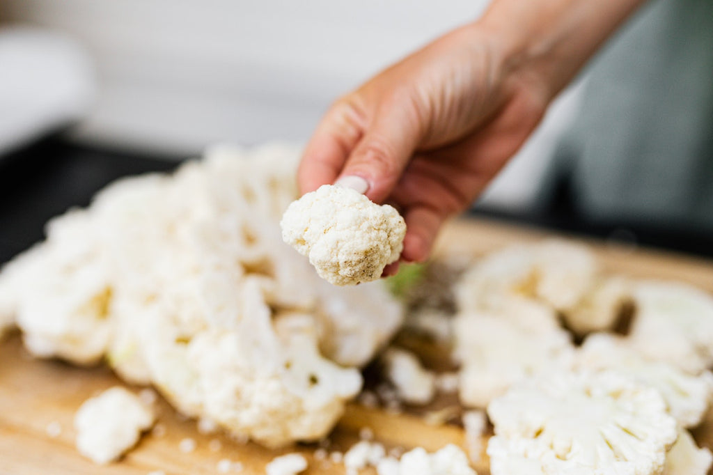 A close-up shot of a cauliflower rosette with cuts of cauliflower on a wooden cutting board in the background.