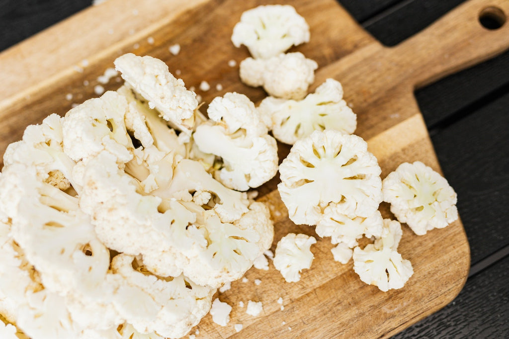 A photo of different cuts of cauliflower on a wooden cutting board.