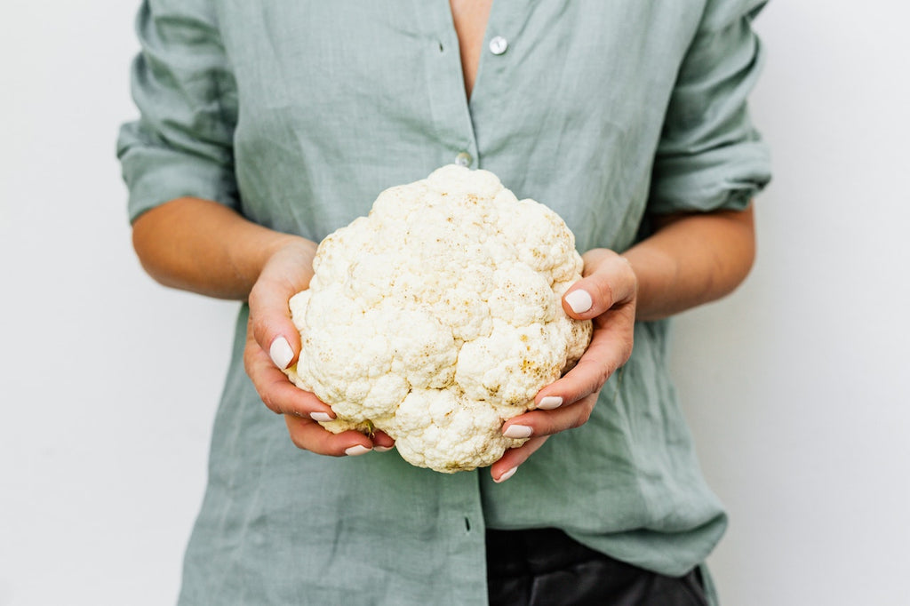 Shot of a girl wearing green buttoned top holding a fresh cauliflower.