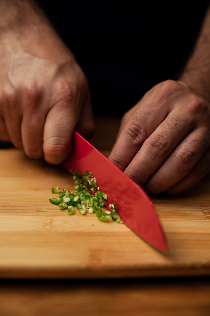 A person slicing green pepper into bits using a red nknife