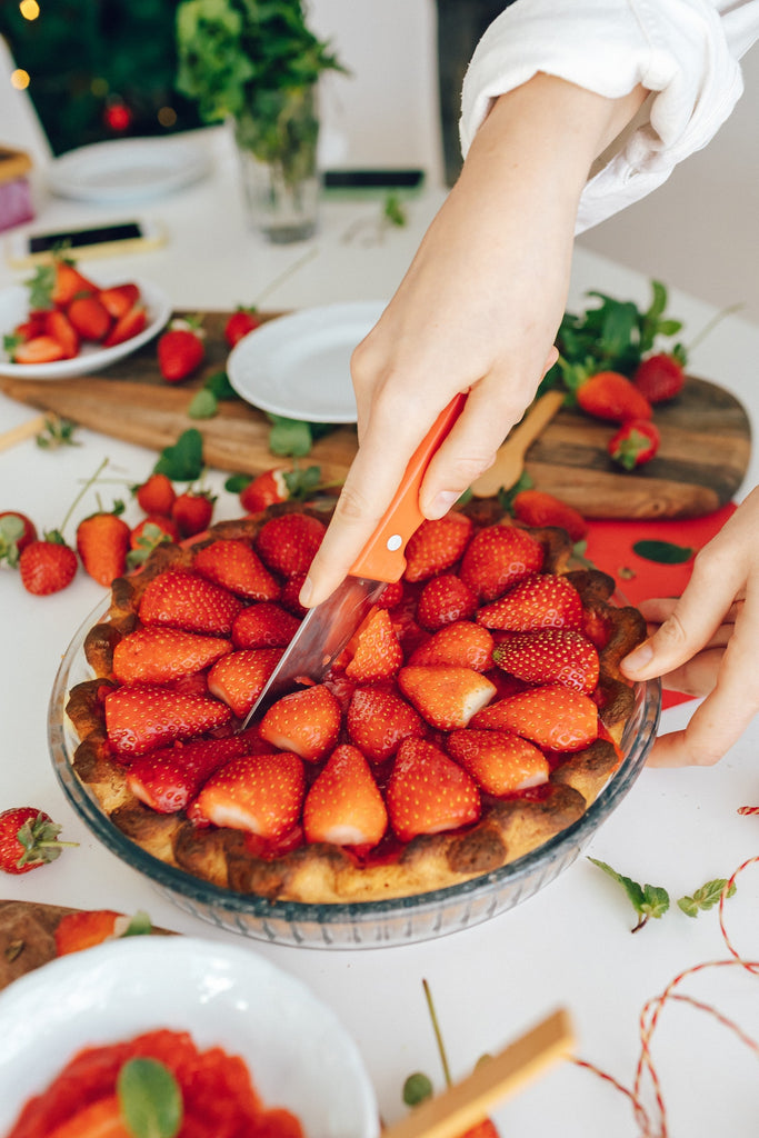 Person slicing a strawberry pie on a glass bowl
