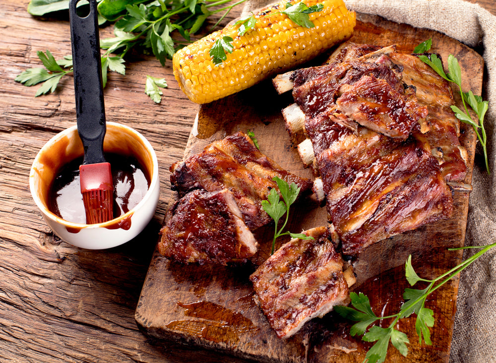 A rack of ribs on a cutting board next to a piece of corn on the cob