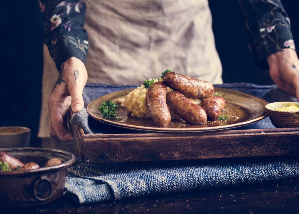 Close up of tattooed hands carrying a tray with a plate of bangers and mash