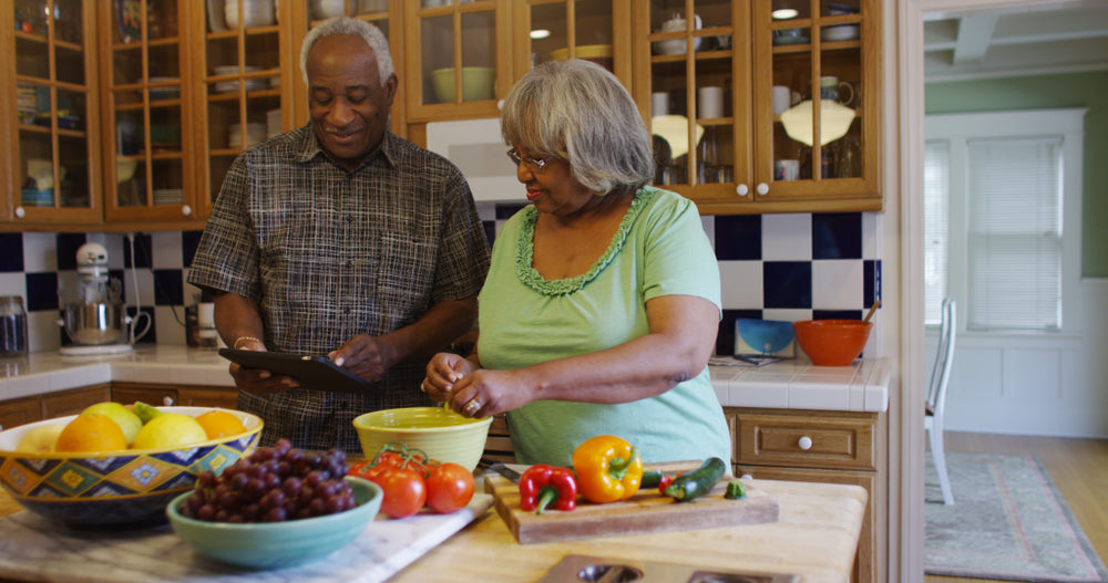 Elderly couple smiling in the kitchen as they prepare a meal using an ipad for directions