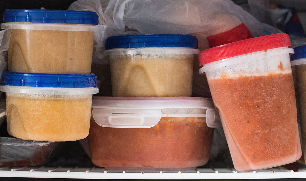5 plastic containers of sauce in a home freezer with more food in the background