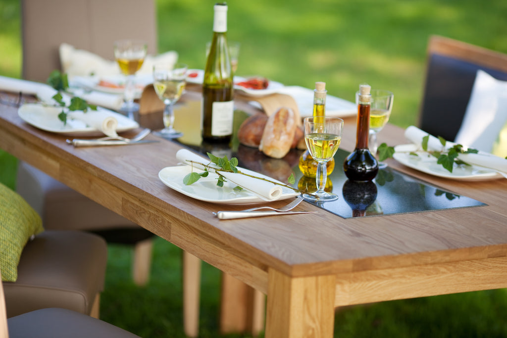 Outdoor wooden table on grass set for dinner with plates, wine glasses and drinks